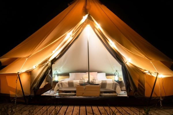 Tent interior and exterior with lamps, bed and furniture at glamping, night